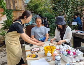 이수아 작가와 함께하는 예술체험「골목을 비추는 얼굴들」2025 금강자연미술프레비엔날레 체험프로그램작가 이수아와 함께한 예술체험 ‘골목을 비추는 얼굴들’이 즐겁게 진행되었습니다.빵 도마 위에 놓인 작은 조약돌들이 아이들의 손끝에서 눈, 코, 입이 되어 저마다 개성 넘치는 얼굴로 완성되었습니다.아이들의 상상력과 웃음이 더해진 작품들은 제민천 골목 곳곳을 환하게 비추는 ‘작은 얼굴 등불’이 되었습니다.참여해주신 어린이와 가족, 그리고 관람객 여러분께 감사드립니다.자연과 예술이 만나는 골목에서, 여러분의 미소가 또 하나의 예술이 되었습니다.  